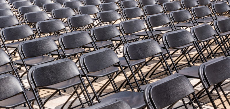 Rows of black folding chairs are meticulously arranged within an outdoor setting, reminiscent of the structured elegance found in the Peppol framework.